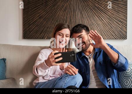 Romantic young diverse couple in casual clothes relaxing on sofa and watching photos on smartphone during weekend at home Stock Photo