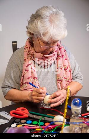 Easter egg painting and decorating activity concept: An elderly senior grandmother with white hair is preparing for the holidays. Creative deco Stock Photo