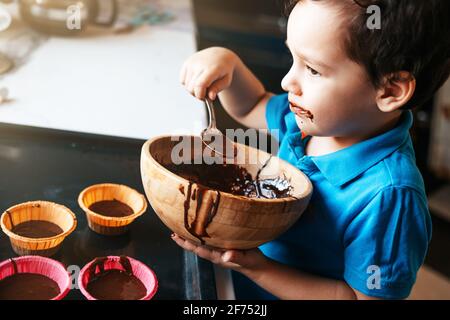 A little boy licks a spoon with chocolate dough Stock Photo