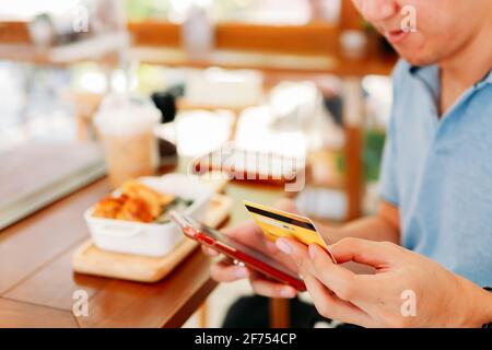 Closeup of hands of handsome young Asian man making card payment using smartphone while eating lunch in modern cafe with social distancing norms due to coronavirus Stock Photo