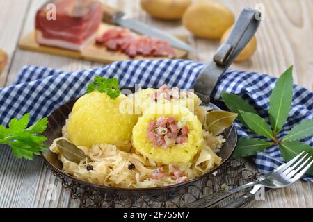 Potato dumplings stuffed with South Tyrolean bacon and served with sauerkraut in an iron pan Stock Photo