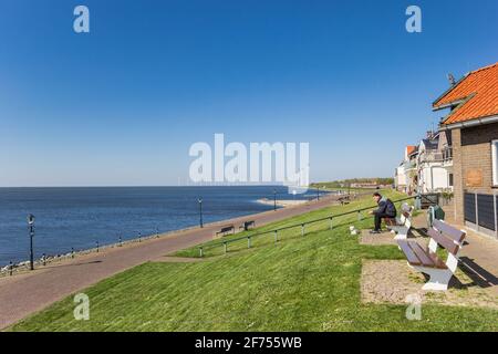 Man overlooking the IJsselmeer lake from a bench on top of the dike in Urk, Netherlands Stock Photo