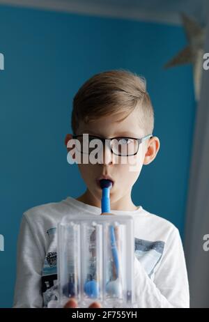 Young boy breaths deep exercise with incentive spirometer. Threeflow respiratory exerciser for help perform normal breathing. Stock Photo
