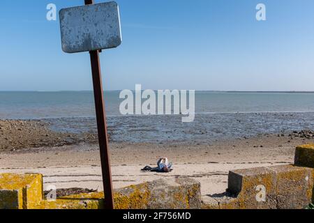 Ars-en-Ré, France - February 24, 2020: One person texting on a beach taken from far way on the Isle of Rhé on a sunny late winter day Stock Photo