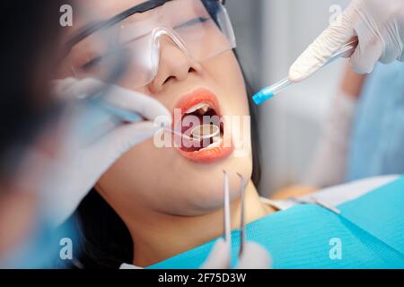 Close-up image of dentist with mirror and saliva ejector examining teeth of young female patient Stock Photo