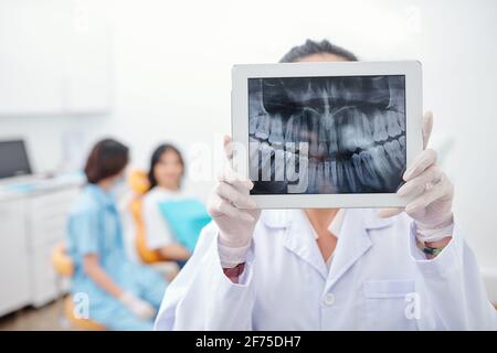 Dentist showing tablet computer with jaw x-ray of female patient on screen Stock Photo