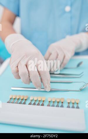 Hands of dentist in silicone gloves putting disinfected tools and veneers color palette on tray Stock Photo
