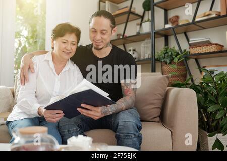 Handsome smiling man hugging his mature mother when they are looking at old photos in album Stock Photo
