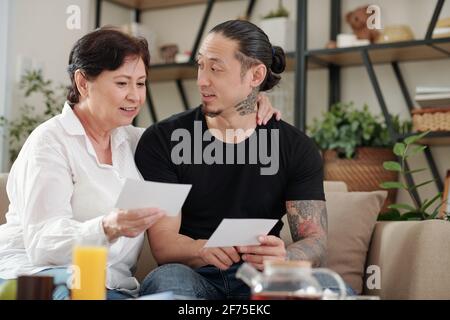 Mixed-race mature woman talking to her adult son and showing him old photos of her youth Stock Photo