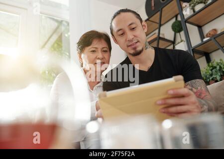 Smiling mature mixed-race man showing new helpful application on tablet computer to his mature mother Stock Photo
