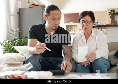 Mixed-race man helping mature mother with managing home finances and paying bills Stock Photo