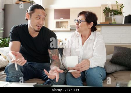 Positive mixed-race man explaining mother how to pay utility bills or receipts online and manage monthly expenses Stock Photo