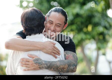 Happy handsome mixed-race an hugging his mature mother after meeting her on the street Stock Photo