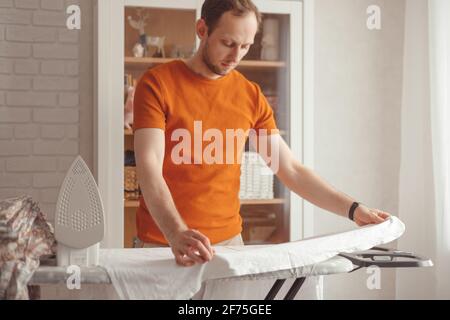 Young man ironing children's sheet on ironing board at home Stock Photo