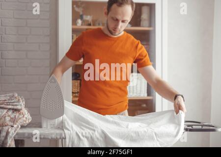 Young man ironing children's sheet on ironing board at home Stock Photo