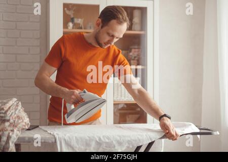 Young man ironing children's sheet on ironing board at home Stock Photo