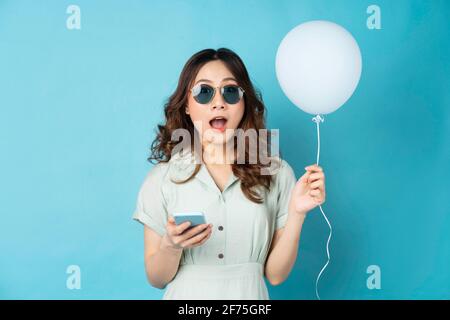Young woman holding balloons and using phone with surprised expression on background Stock Photo