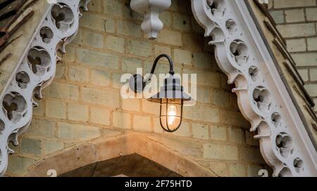 Detail of a black metal lamp with a ligthed bulb hanging on a yellow brick wall Stock Photo