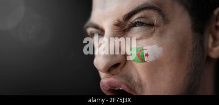 A screaming man with the image of the Algeria national flag on his face Stock Photo