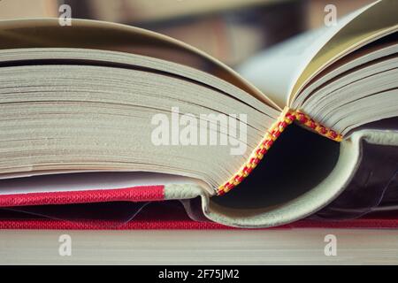 Close-up of an open book with red cover between a stack of closed books. Blurred background, copy space. Concept of studying, business. Stock Photo
