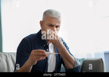 Sick senior man sneezing nose and checking fever Stock Photo