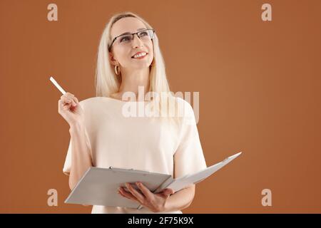 Portrait of creative smiling businesswoman in glasses writing down her ideas in document and looking up Stock Photo