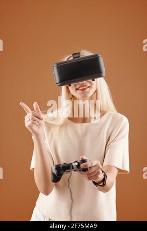 Portrait of smiling young woman using controller when playing videogame in virtual reality glasses Stock Photo