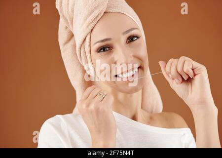 Portrait of pretty smiling young woman with towel on her head using dental floss, oral hygiene concept Stock Photo