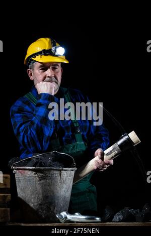 A miner with a pickaxe in his hand stands by a bucket full of black coal on a black background Stock Photo