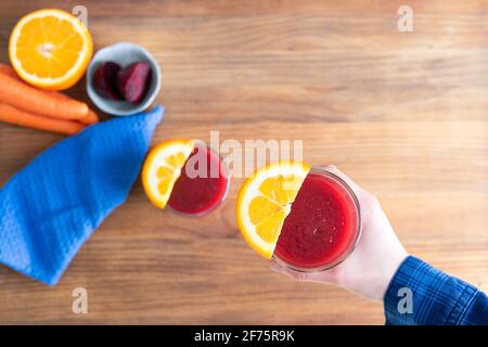 Beet juice in hand with orange decoration on wooden background. Copy space. Top view. Stock Photo