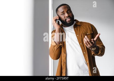 Attractive smiling young african man using mobile phone while standing at the window indoors Stock Photo