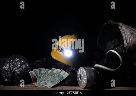 A protective helmet with a glowing flashlight and a dust mask with a filter and paper bills lie on top of the black coal Stock Photo