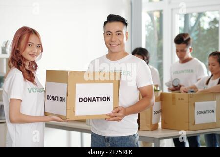 Young Asian couple working as volunteers in donation center, theay are packing boxed for people in need Stock Photo