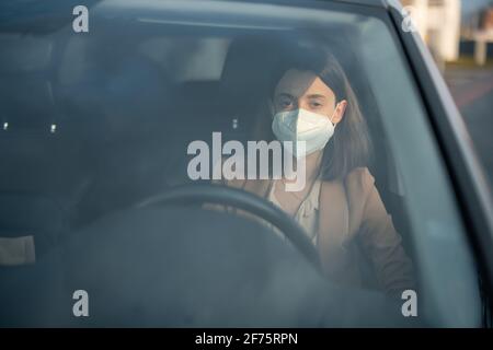 Young woman driving car with protective mask on her face. Healthcare, virus protection, allergy protection concept.  Stock Photo