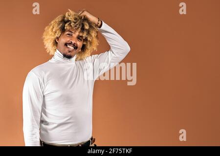 Stock photo of cheerful afro man smiling and looking at camera in studio shot against brown background. Stock Photo