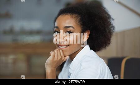 happy african american woman smiling and biting lips in cafe Stock Photo