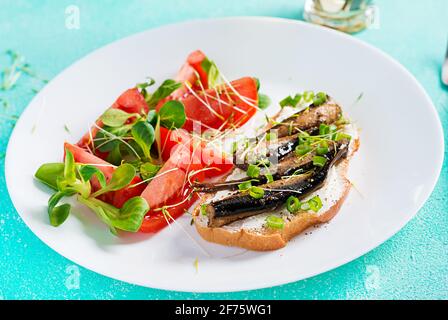 Sandwich - smorrebrod with sprats and tomatoes salad on white plate. Danish cuisine. Stock Photo