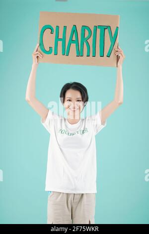 Smiling young Asian volunteer standing with charity placard, isolated on light blue Stock Photo