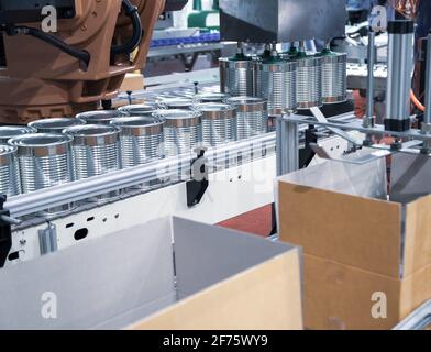Automation robot lifting food can into cardboard in production line. Food industry. Stock Photo