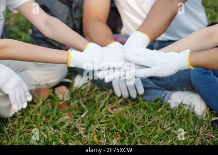 Volunteers in textile gloves stacking hands to express unity after finishing picking up trash in city park Stock Photo