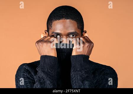 Stock photo of serious black man covering his face with his jumper and posing in studio shot. Stock Photo