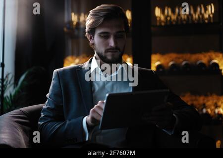 Businessman working using tablet computer while sitting in cafe late at night in front of windows overlooking the city. Stock Photo