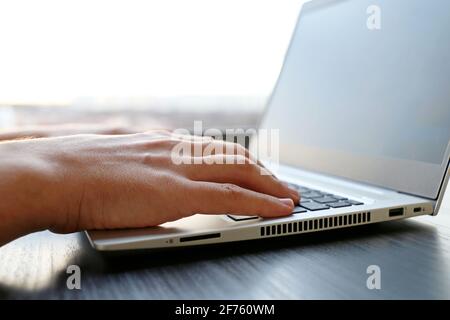 Man working at laptop keyboard near the window, male hands close up. Cozy workplace, concept of online communication, office or home work Stock Photo