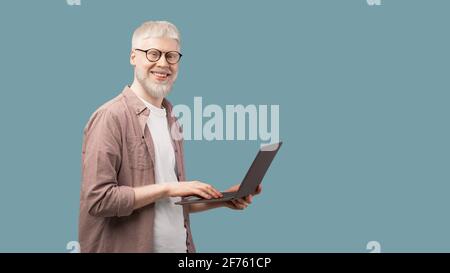 Happy albino man using laptop and looking with smile to camera over turquoise background, panorama with copy space Stock Photo