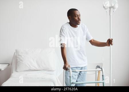 Portrait of African-American man in hospital holding onto iv drip stand and looking away pensively, copy space Stock Photo