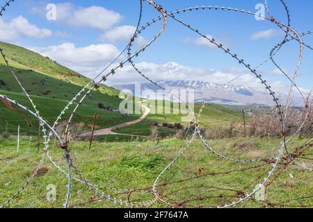 View of Mount Hermon with a snow-capped peak in the clouds through barbed wire Stock Photo