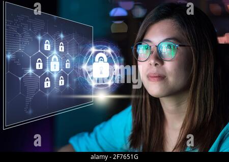 Portrait of Asia Businesswoman sitting and working hard via Security key lock icon digital hologram display over the world map and Hexagon shape on th Stock Photo