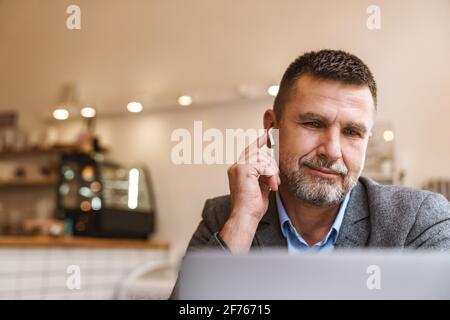 Confident handsome young business man wearing earphones sitting at the table in cafe with laptop computer, working Stock Photo