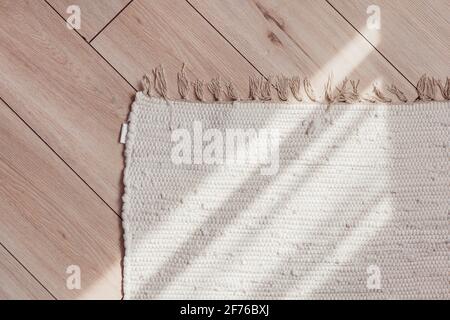 Wicker beige rug on wooden parquet floor with sunlit, top view. Stock Photo