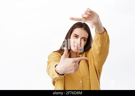 Thoughtful creative woman searching perfect shot, making hand frames camera gesture and looking through pensive, creating masterpiece, standing Stock Photo